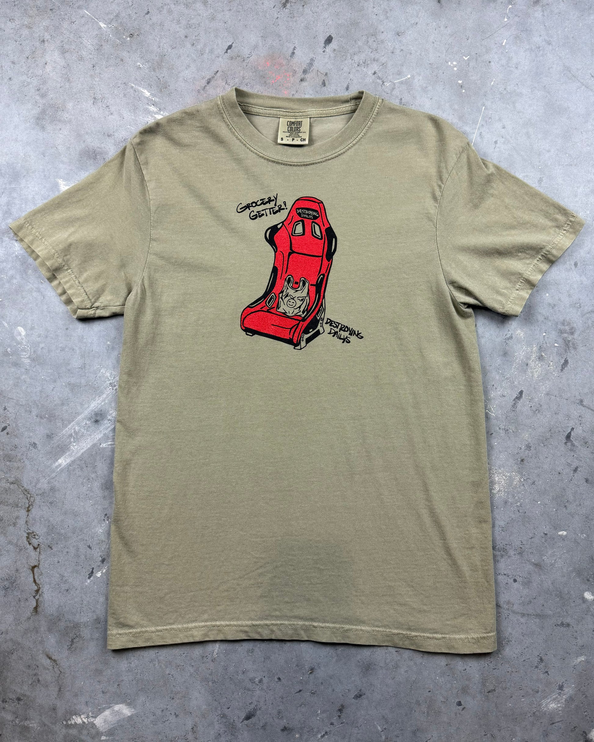 tan 100% cotton t-shirt featuring a hand-drawn red racing seat with a grocery bag and the text "Grocery Getter! Destroying Dailys," perfect for car enthusiasts. Funny car shirt for car enthusiasts. car clothing for car enthusiasts.