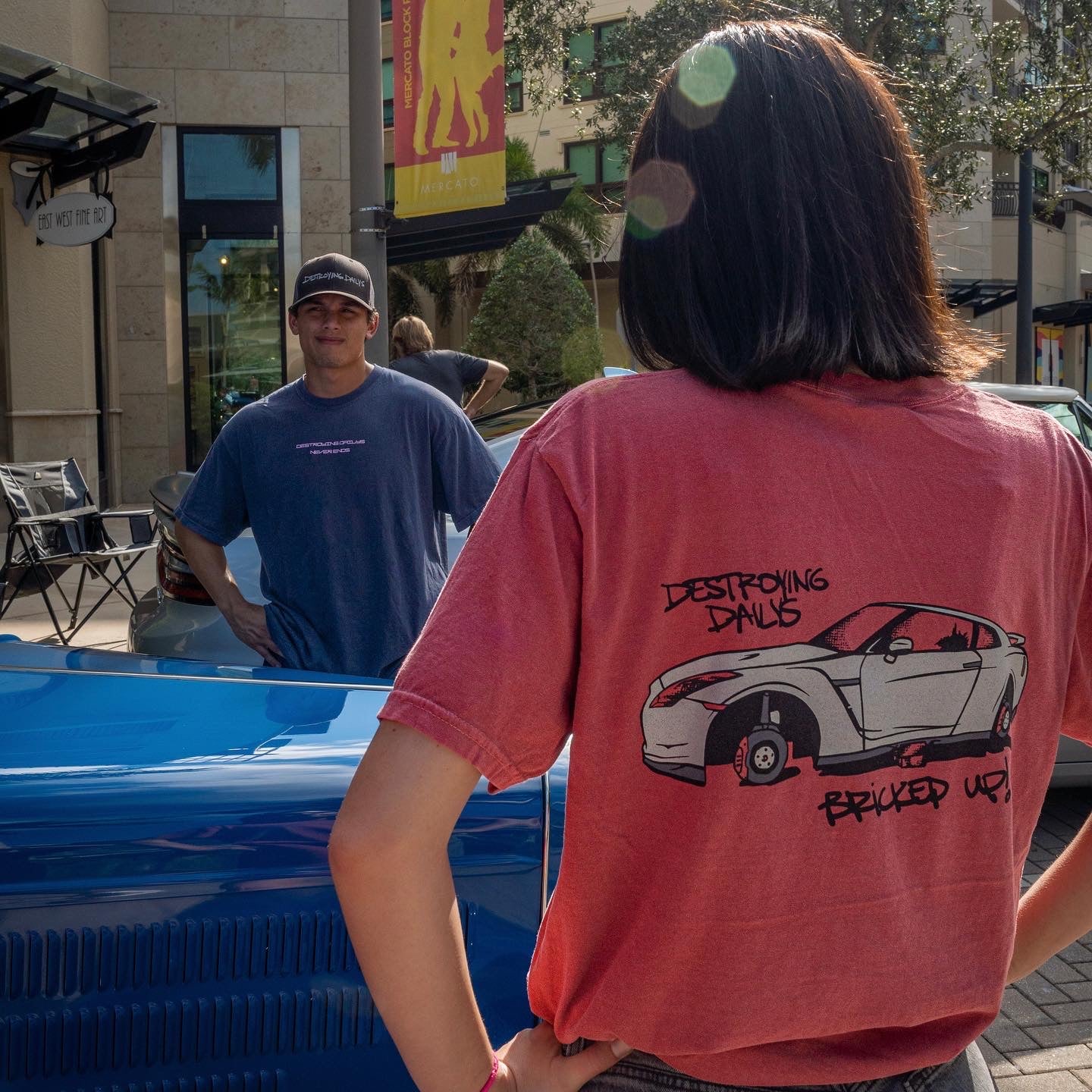 Female model with Red 100% cotton t-shirt featuring a hand-drawn Nissan GTR on bricks with the text "Destroying Dailys Bricked Up!" perfect for JDM enthusiasts. Funny Tee for Car guys back lifestyle photo