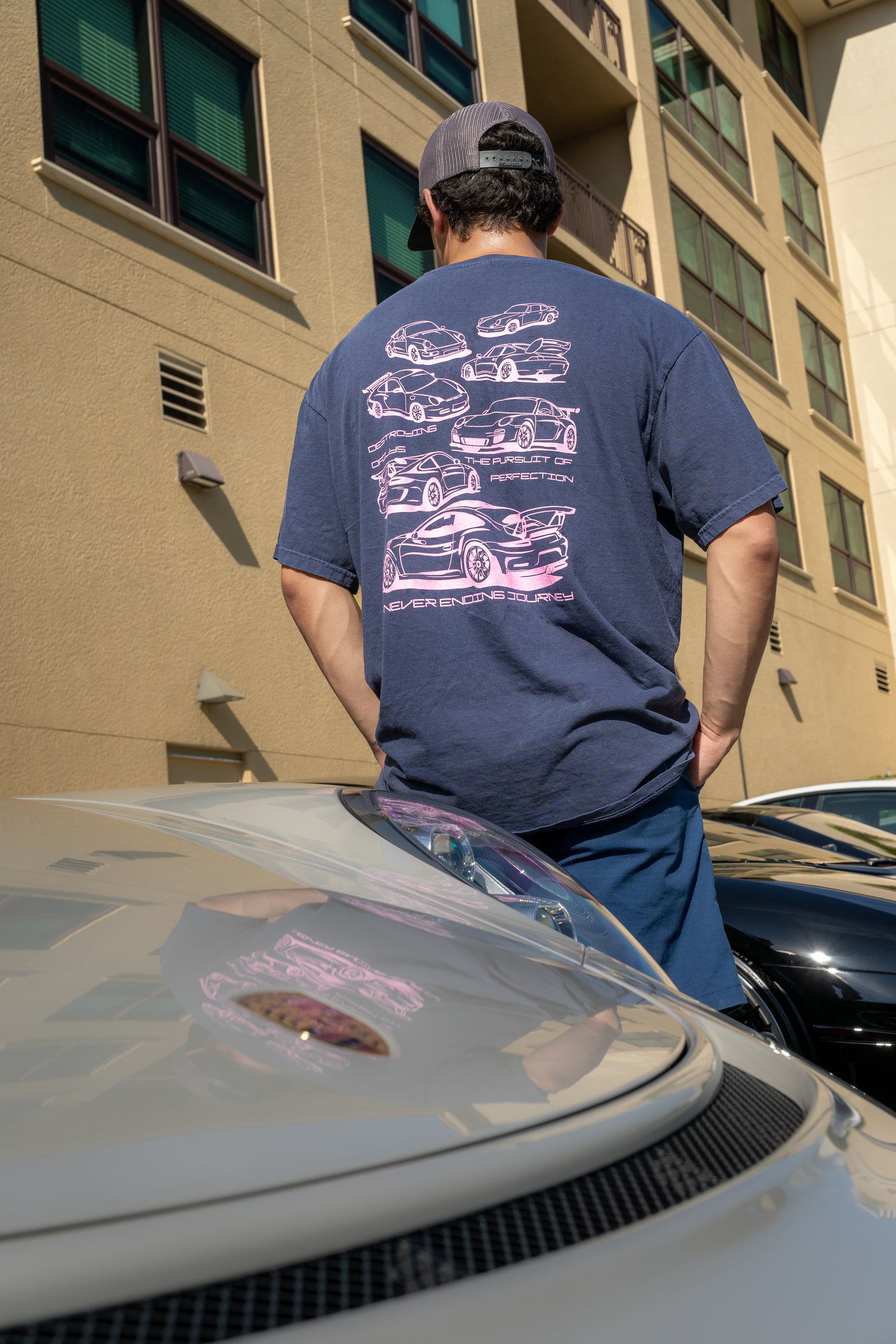 model wearing Navy blue 100% cotton t-shirt featuring hand-drawn Porsche 911 GT3 RS designs with the text "Destroying Dailys The Pursuit of Perfection A Never Ending Journey," perfect for car enthusiasts.