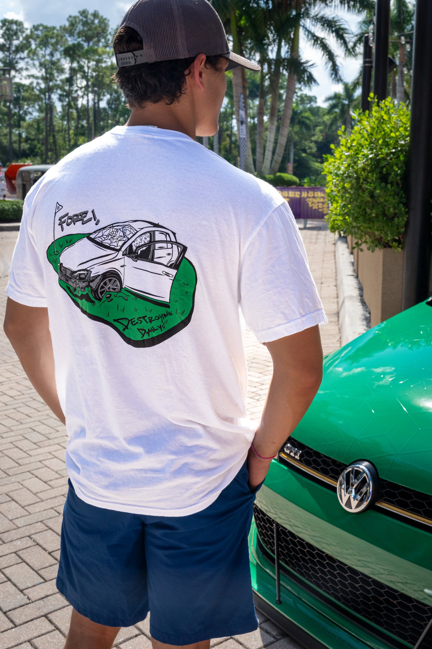 Male model wearing White 100% cotton t-shirt featuring a hand-drawn crashed Golf GTI on a golf course with the text "Fore! Destroying Dailys," perfect for car enthusiasts.