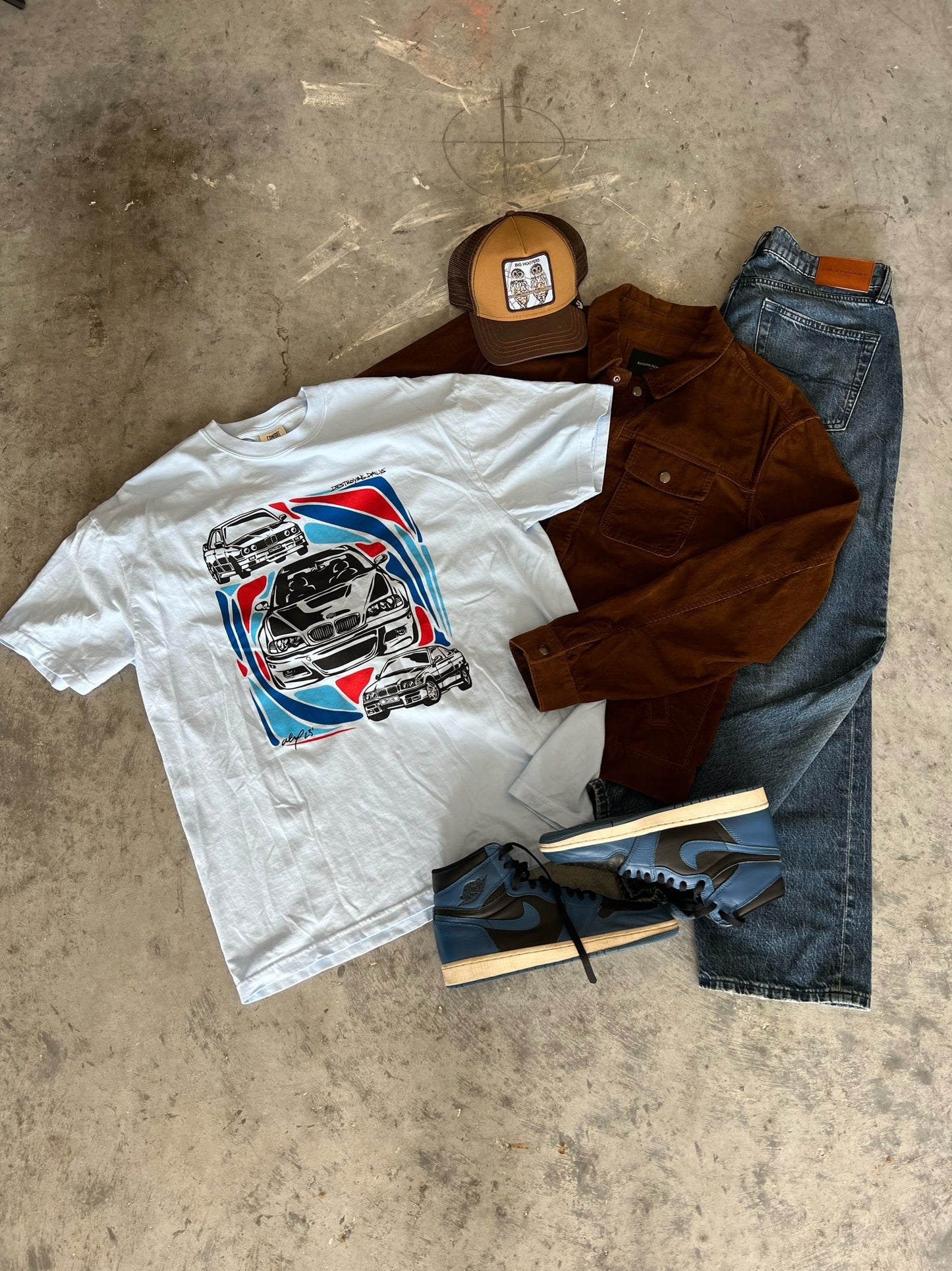  SEO Alt Text Generator Light blue 100% cotton t-shirt featuring hand-drawn BMW E30, E36, and E46 designs with red, blue, and black accents, styled with jeans, brown jacket, and sneakers, ideal for car enthusiasts.