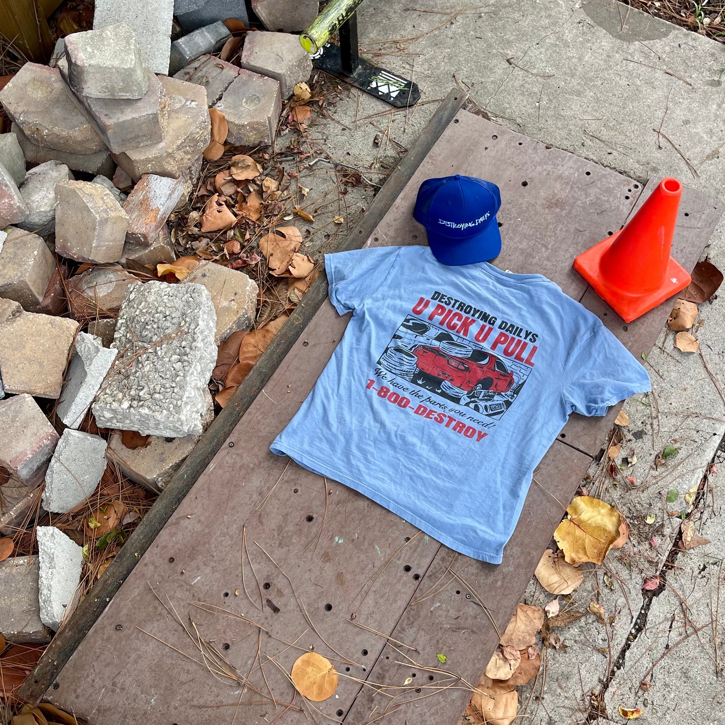 Light blue 100% cotton t-shirt with a JDM Rx-7 graphic and "Destroying Dailys U Pick U Pull 1-800-DESTROY" text, paired with a blue hat, perfect for car enthusiasts.