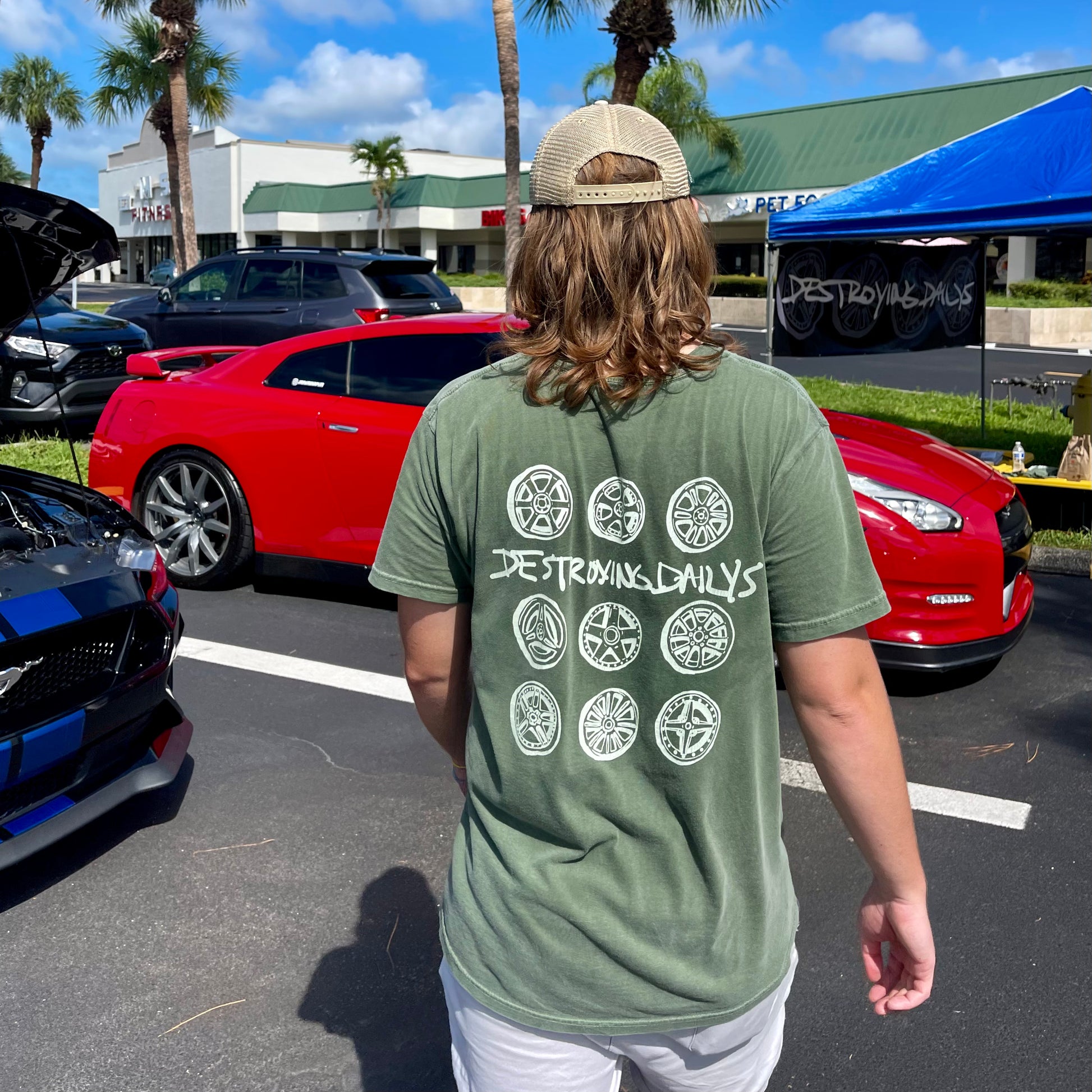 man wearing Green 100% cotton t-shirt featuring hand-drawn JDM wheels and the text "Destroying Dailys" on the back, perfect for JDM fans and car enthusiasts.