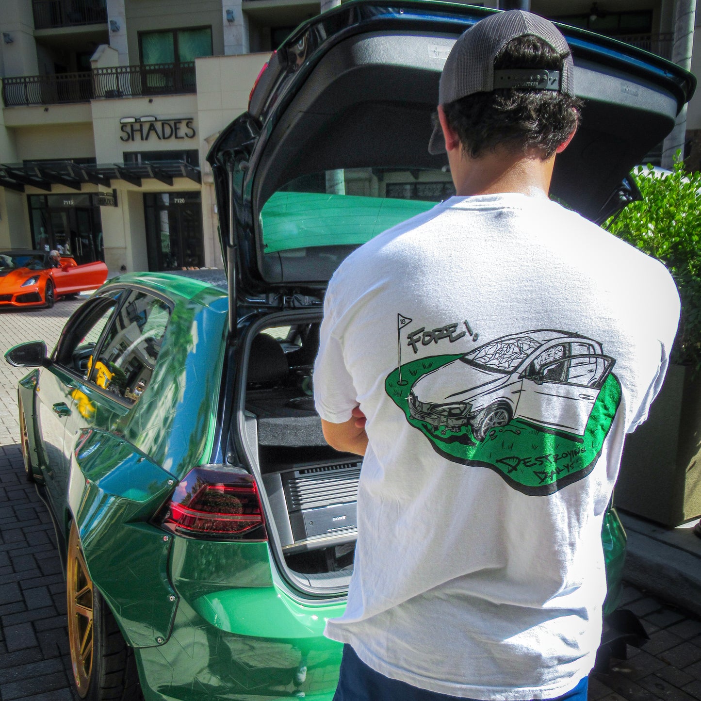 male model in front of golf gti wearing White 100% cotton t-shirt featuring a hand-drawn crashed Golf GTI on a golf course with the text "Fore! Destroying Dailys," perfect for car enthusiasts.