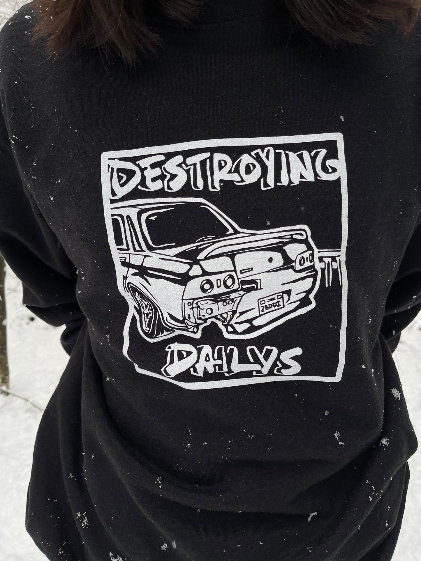 Female model in snow wearing  Black crewneck sweatshirt made of 50/50 cotton and polyester blend featuring a hand-drawn JDM Skyline R32 with the text "Destroying Dailys," perfect for car enthusiasts. JDM sweatshirt for car guys, Nissan Skyline sweatshirt