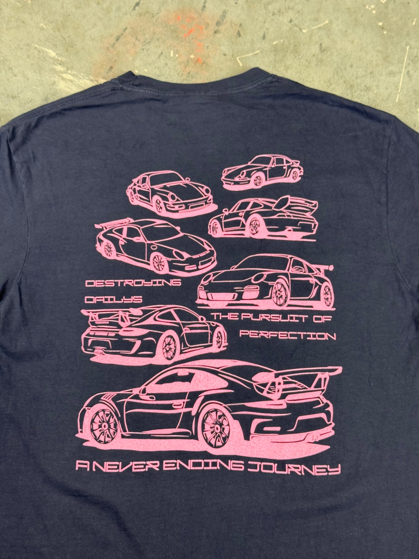 close up view of Navy blue 100% cotton t-shirt featuring hand-drawn Porsche 911 GT3 RS designs with the text "Destroying Dailys The Pursuit of Perfection A Never Ending Journey," perfect for car enthusiasts.