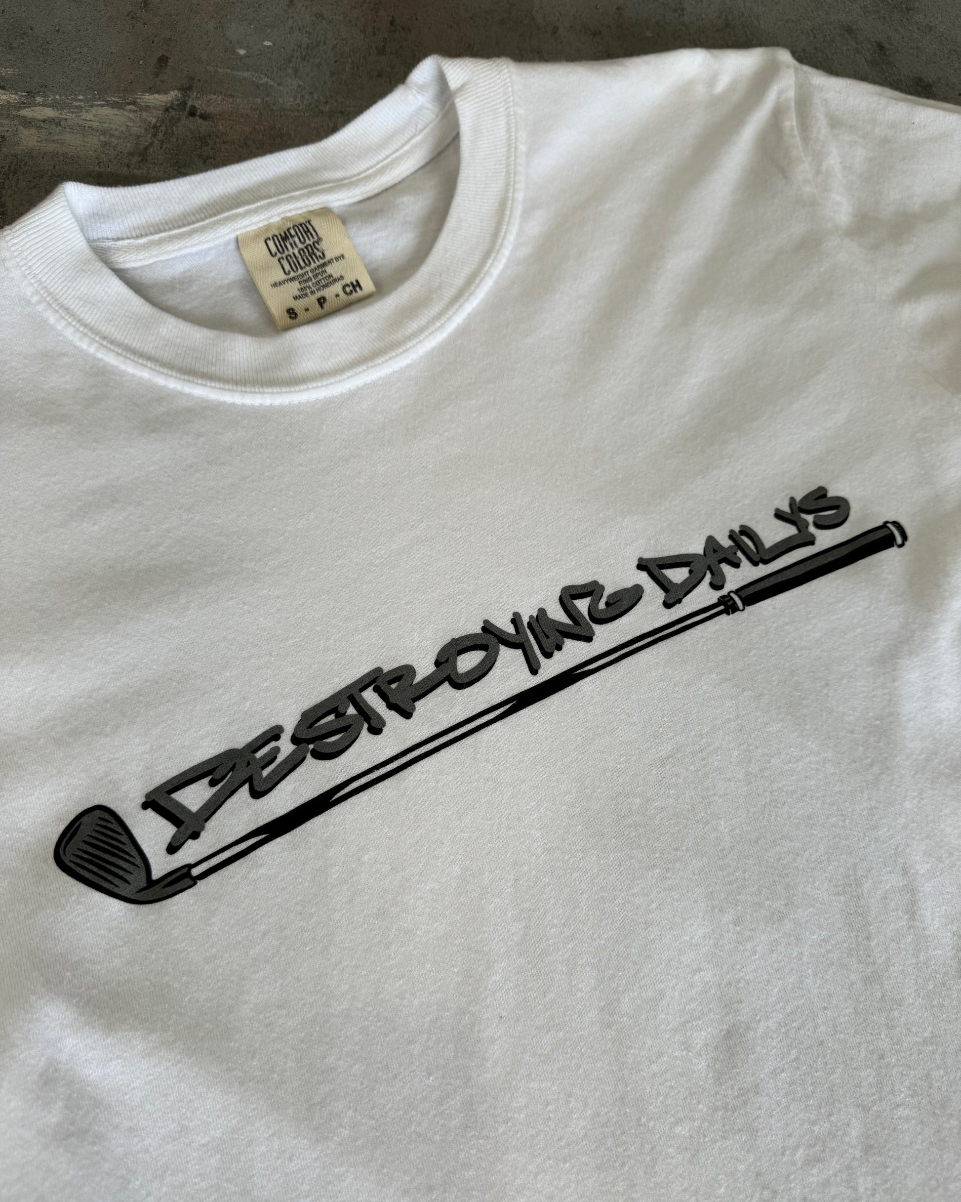 close up front view of comfort color tag on White 100% cotton t-shirt featuring a hand-drawn crashed Golf GTI on a golf course with the text "Fore! Destroying Dailys," perfect for car enthusiasts.