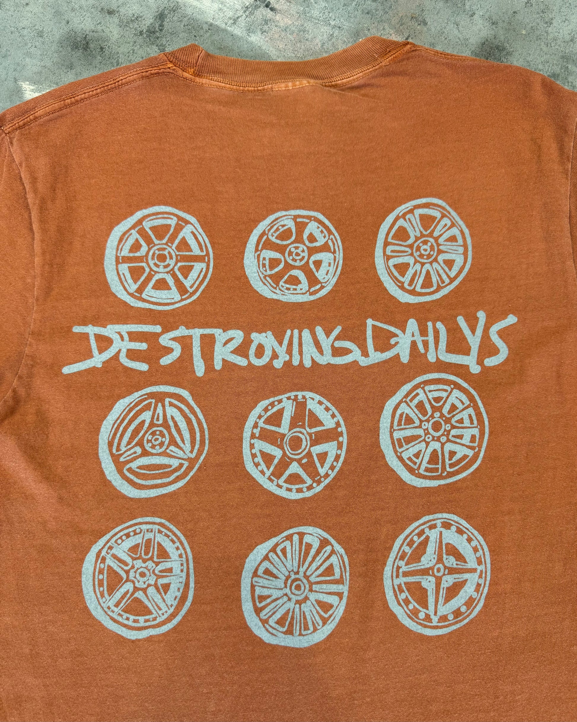 Orange 100% cotton t-shirt featuring a hand-drawn design of JDM wheels with the text "Destroying Dailys," perfect for car enthusiasts. close up detailed view