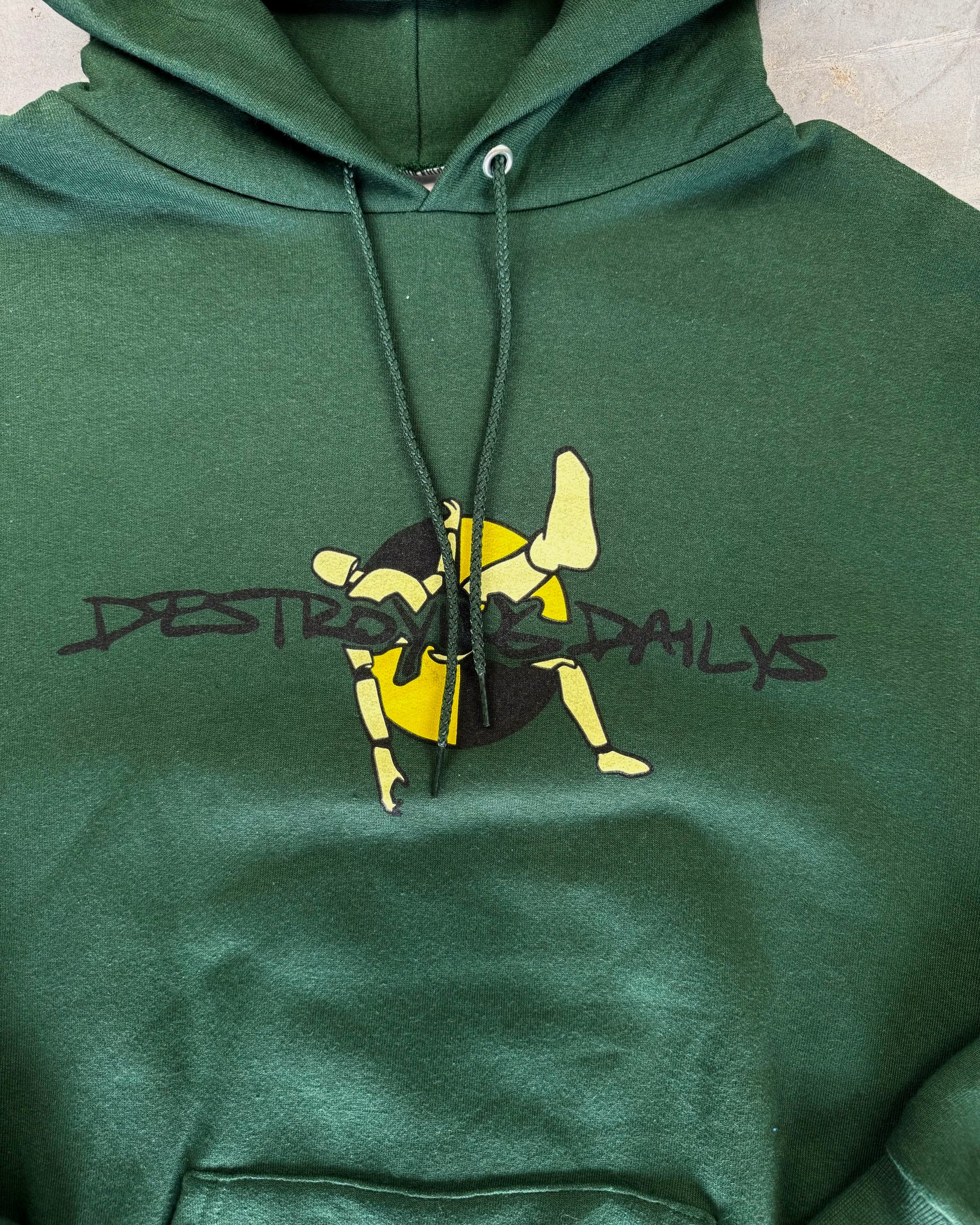 front detailed photo of Dark green hoodie made of 50/50 cotton and polyester blend featuring a hand-drawn crash test dummy with the text "Be A Dummy... Destroy the Daily: Destroying Dailys," perfect for modified car enthusiasts.