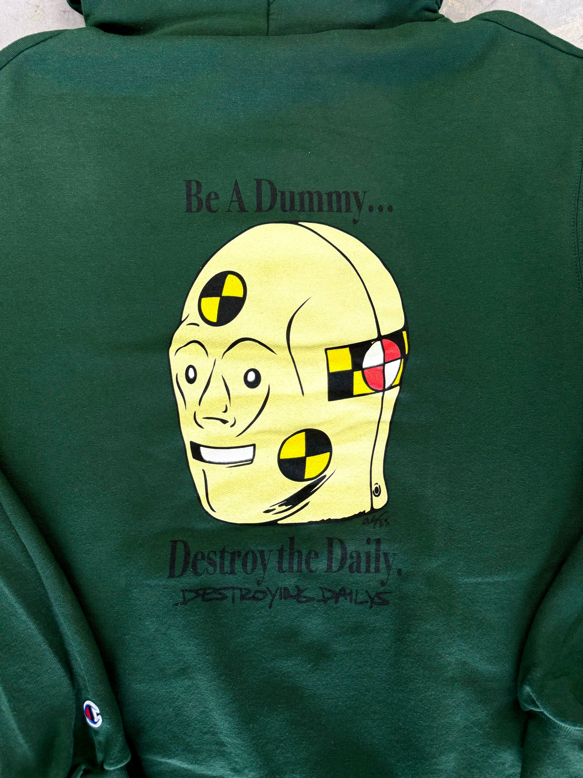 Detailed photo of Dark green hoodie made of 50/50 cotton and polyester blend featuring a hand-drawn crash test dummy with the text "Be A Dummy... Destroy the Daily: Destroying Dailys," perfect for modified car enthusiasts.