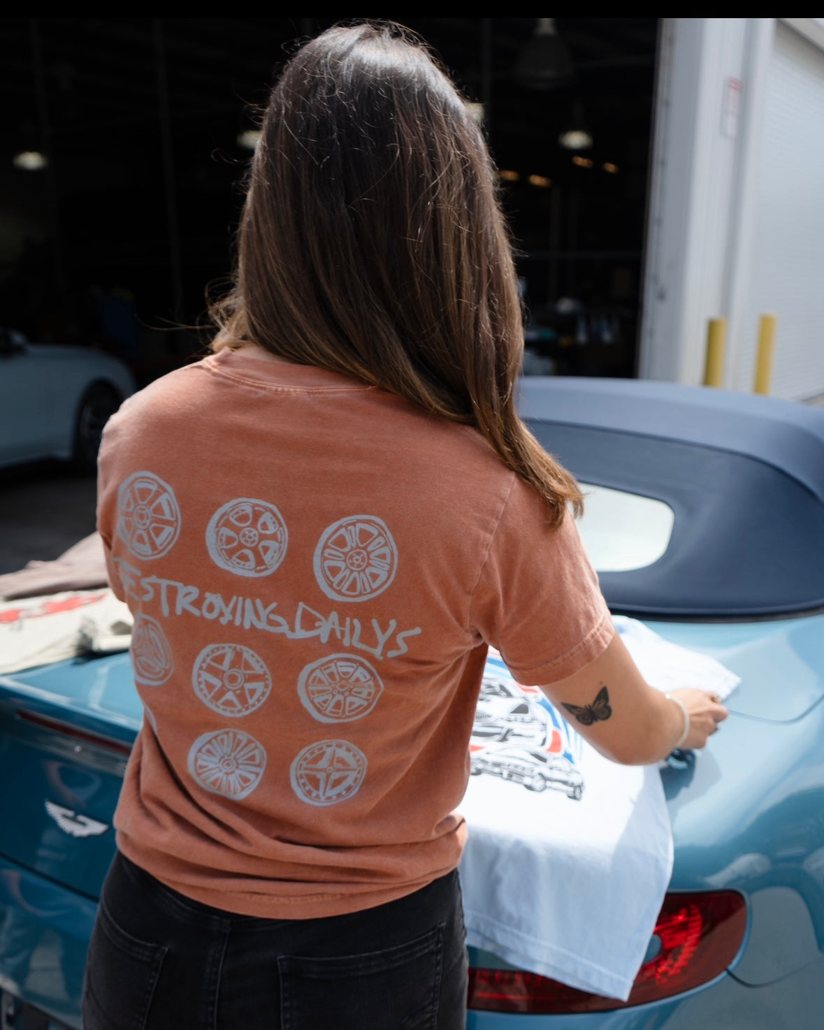 Female Model wearing Orange 100% cotton t-shirt featuring a hand-drawn design of JDM wheels with the text "Destroying Dailys," perfect for car enthusiasts.