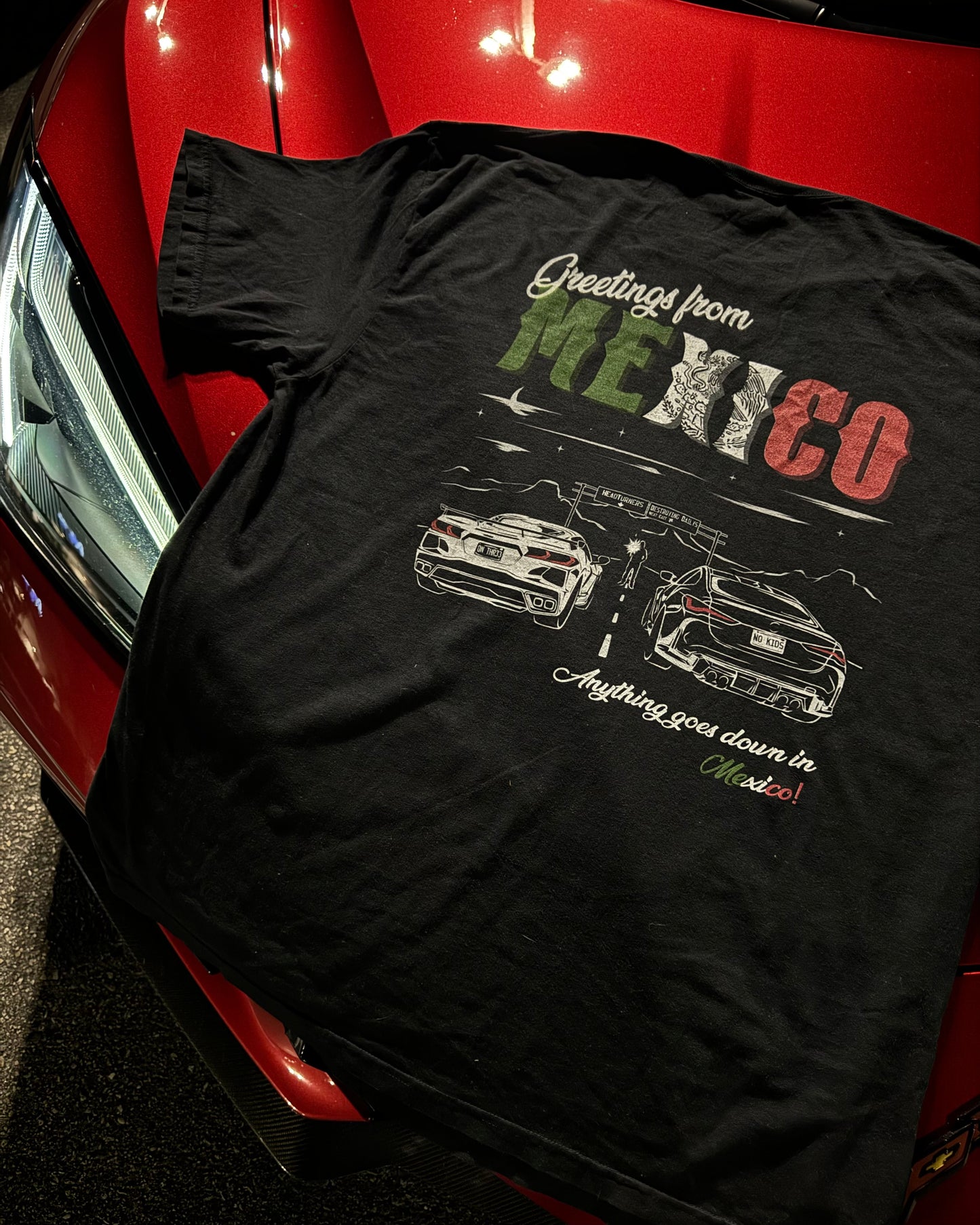 detailed Black 100% cotton t-shirt featuring a hand-drawn Mexico racing scene with the text "Greetings from Mexico, Anything goes down in Mexico!" perfect for car enthusiasts. Mexico Racing T Shirt. Mexico racing corvette shirt.