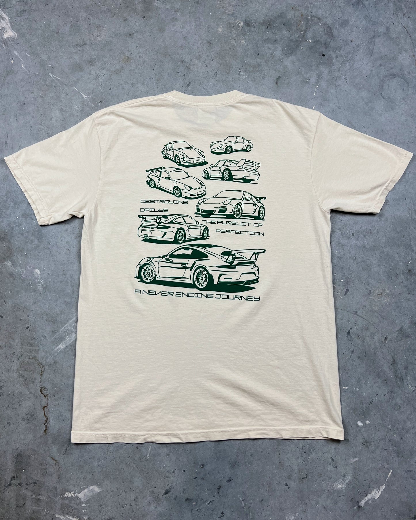 White 100% cotton t-shirt featuring green hand-drawn Porsche 911 GT3 RS designs with the text "Destroying Dailys The Pursuit of Perfection A Never Ending Journey," perfect for car enthusiasts.