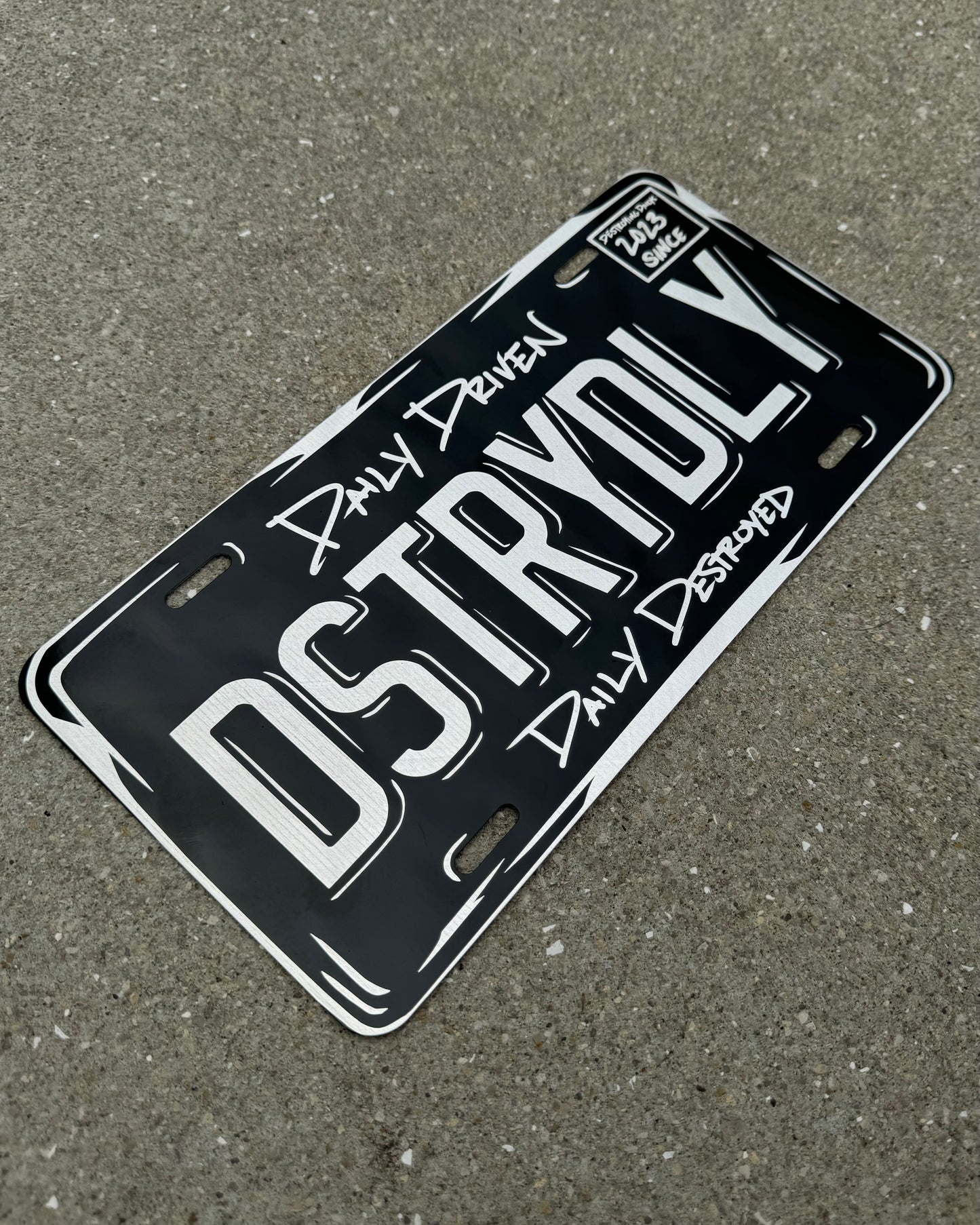 12x6 inch aluminum vanity plate featuring "DSTRYDLY" text with "Daily Driven, Daily Destroyed" and "Destroying Dailys Since 2023," perfect for car enthusiasts. hang up in garage or car, car room decoration, car garage decoration