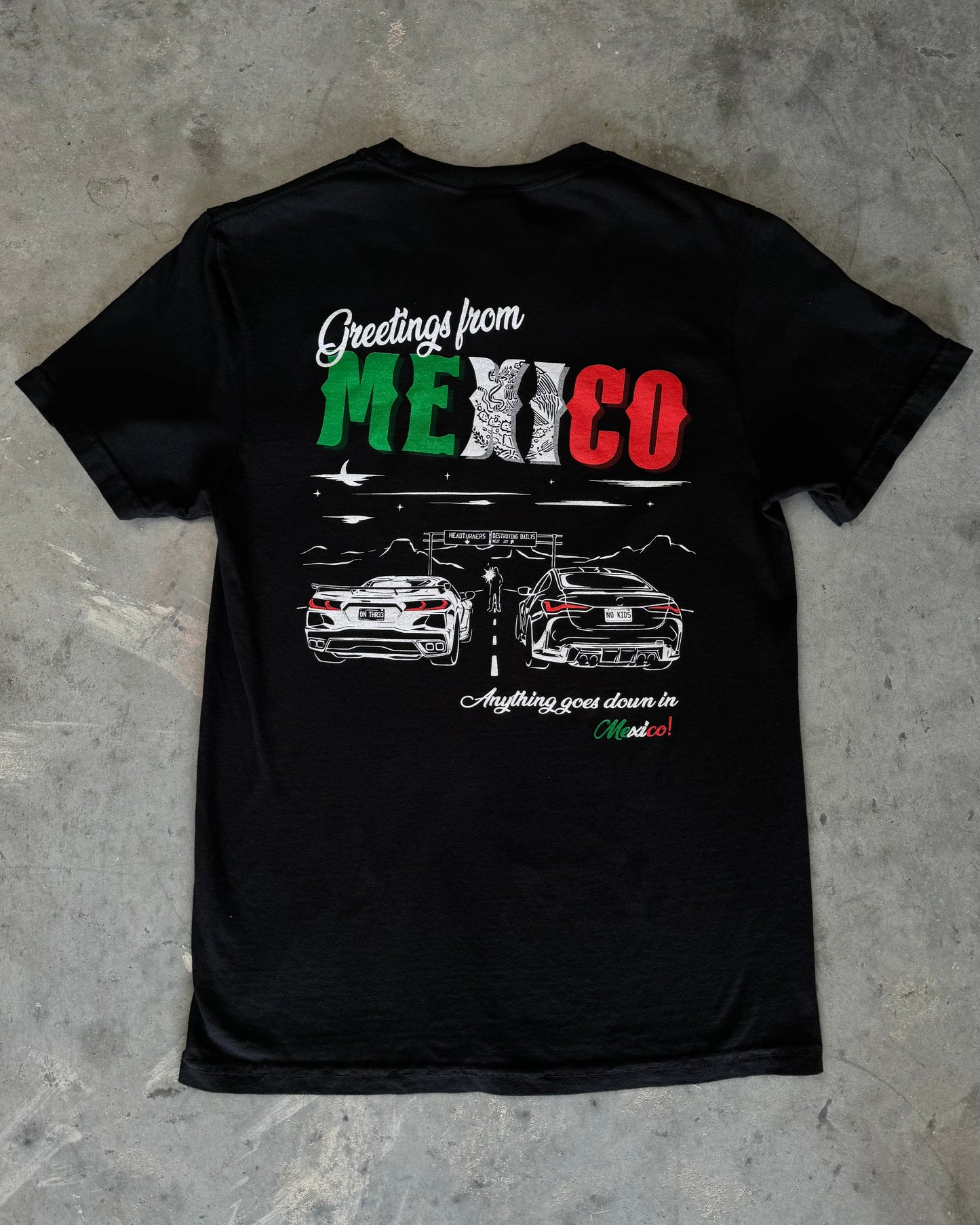 Black 100% cotton t-shirt featuring a hand-drawn Mexico racing scene with the text "Greetings from Mexico, Anything goes down in Mexico!" perfect for car enthusiasts. Mexico Racing T Shirt. Mexico racing corvette shirt. Detailed photo of mexico racing tee