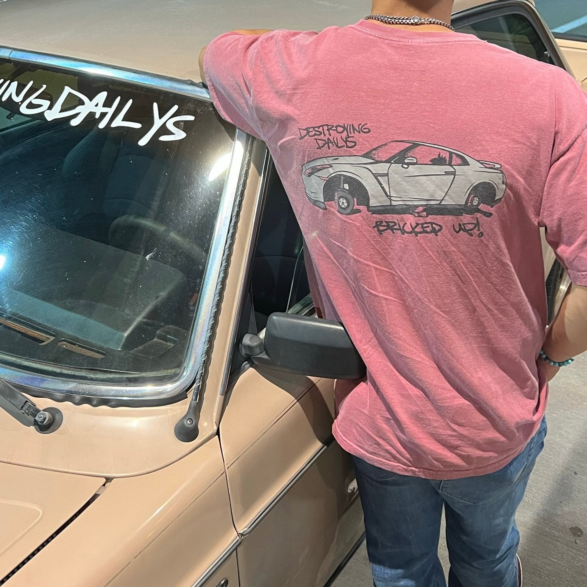 model wearing Red 100% cotton t-shirt featuring a hand-drawn Nissan GTR on bricks with the text "Destroying Dailys Bricked Up!" perfect for JDM enthusiasts. Funny Tee for Car guys