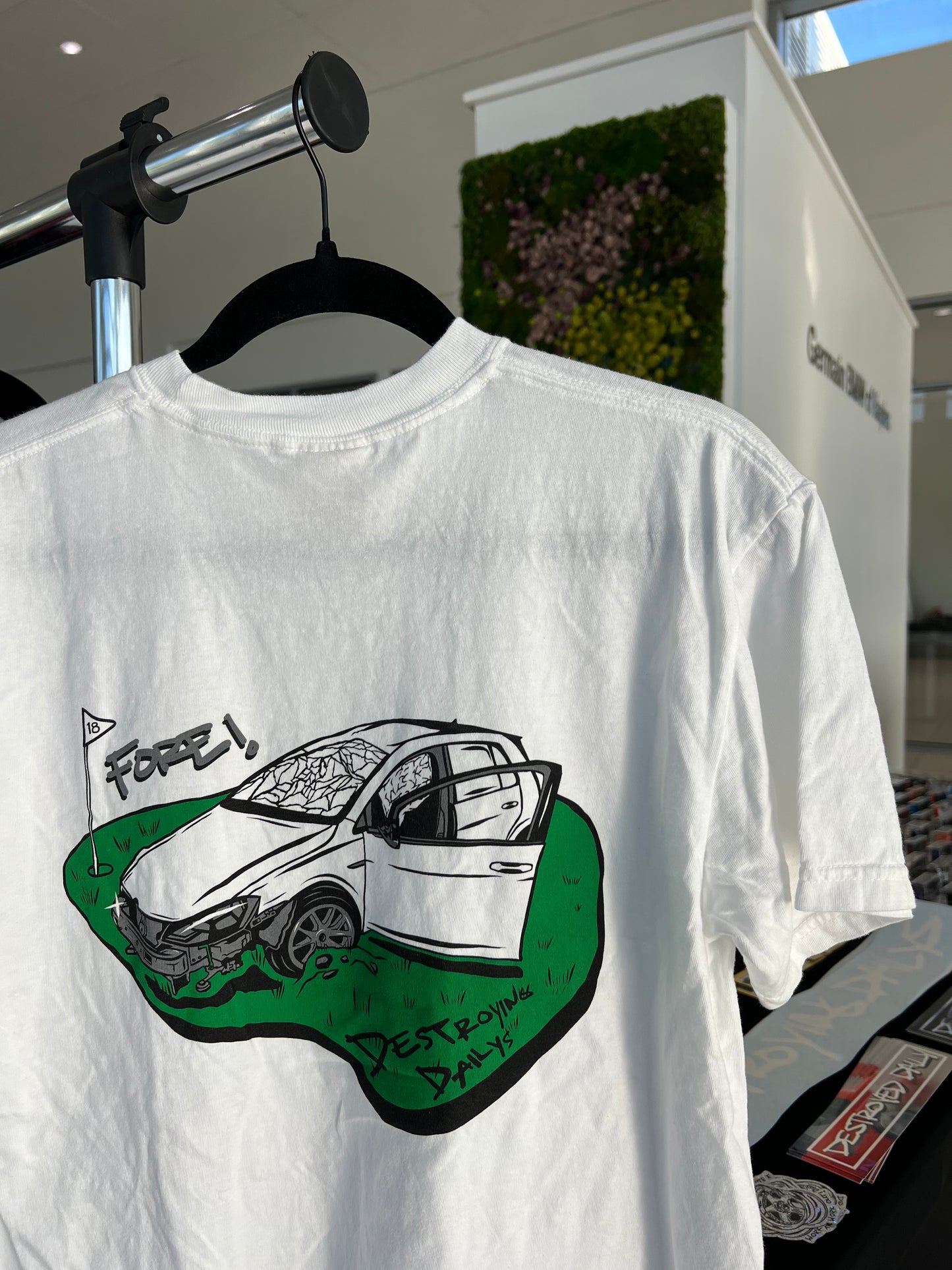 lifestyle photo of back of White 100% cotton t-shirt featuring a hand-drawn crashed Golf GTI on a golf course with the text "Fore! Destroying Dailys," perfect for car enthusiasts.